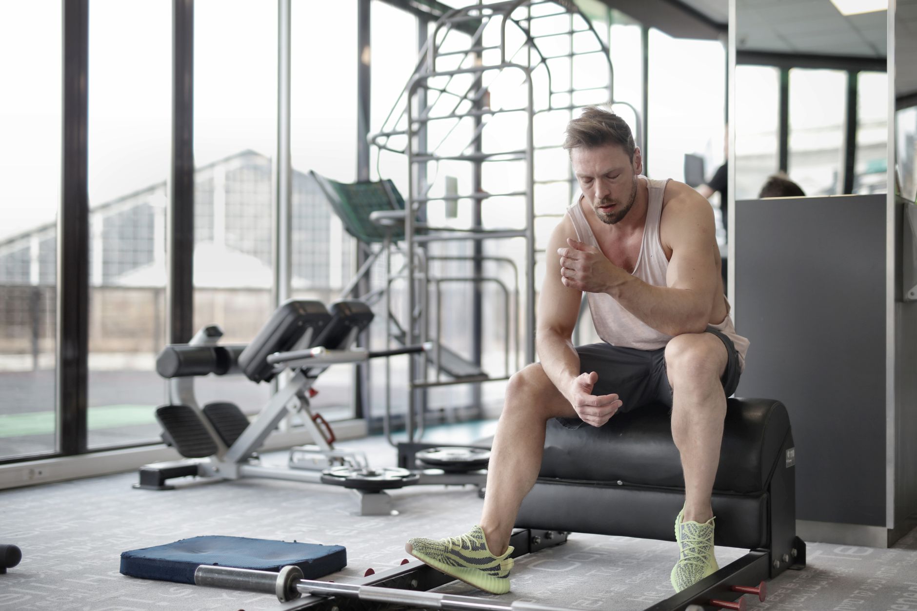 Tired young muscular male athlete in casual sportswear and sneakers sitting on bench and resting after intense weightlifting